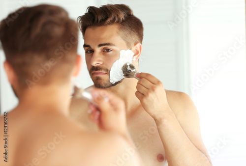 Young man shaving and looking into mirror