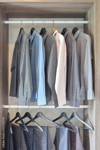 row of colorful shirts and pants hanging in wooden wardrobe