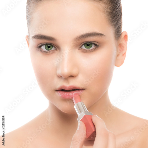 Portrait of beautiful young brunette woman with clean face. Beauty spa model girl with perfect fresh clean skin applying lipstick. Youth and skin care concept. Isolated on a white background.