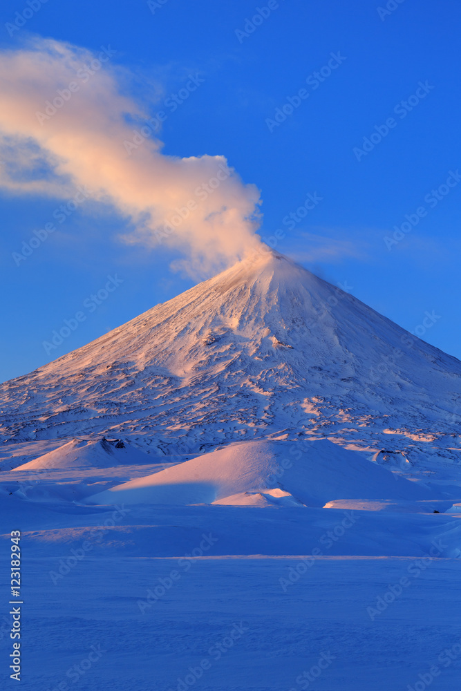 Picturesque winter volcanic landscape of Kamchatka Peninsula: view of eruption active Klyuchevskoy Volcano at sunrise. Eurasia, Russia, Far East, Kamchatsky Region, Klyuchevskaya Group of Volcanoes.