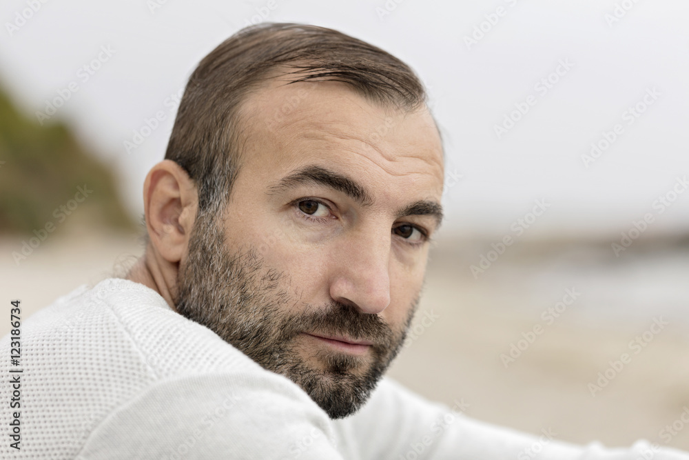 Male (brunette) with a beard in a white sweater looking at the s