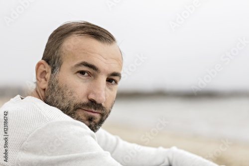 Male (brunette) with a beard in a white sweater looking at the s