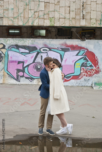 Just married loving hipster couple in wedding dress and suit outdoor in city setting against colorful graffiti wall. Happy bride and groom walking running and dancing. Romantic Married young family. 