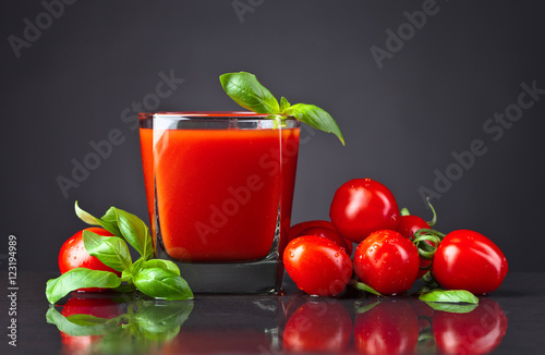 tomato juice with tomatoes and green basil on black table