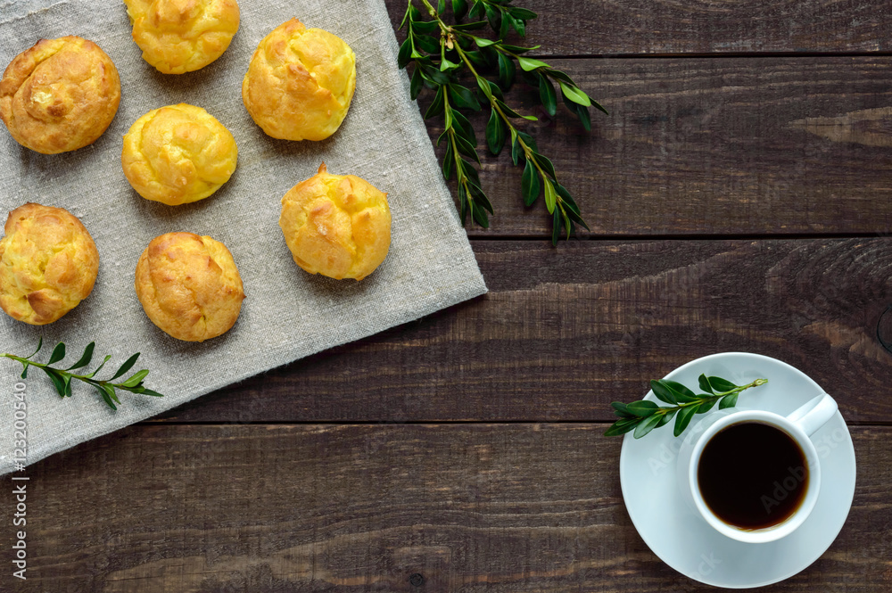 Freshly baked buns eclairs and a cup of coffee (espresso) on a dark wooden background. Light breakfast. The top view. Freshly baked buns eclairs and a cup of coffee (espresso) on a dark wooden background. Light breakfast. The top view.