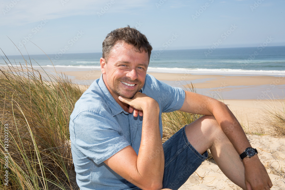 Handsome and confident man smiling and sitting at the beach