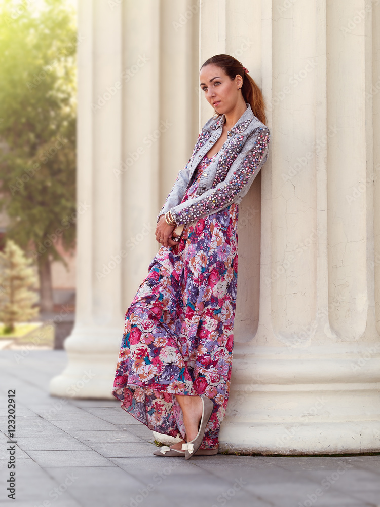 Young girl with brown hair and green eyes, dressed in long dress and jeans jacket, is standing in front of the stone column Young girl with brown hair and green eyes, dressed in long dress and jeans jacket, is standing in front of the stone column