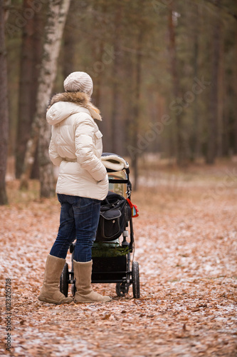 Young woman walking with a stroller in the forest. Mother with a child. Girl with carraige ourdoors. Lifestyle concept photo