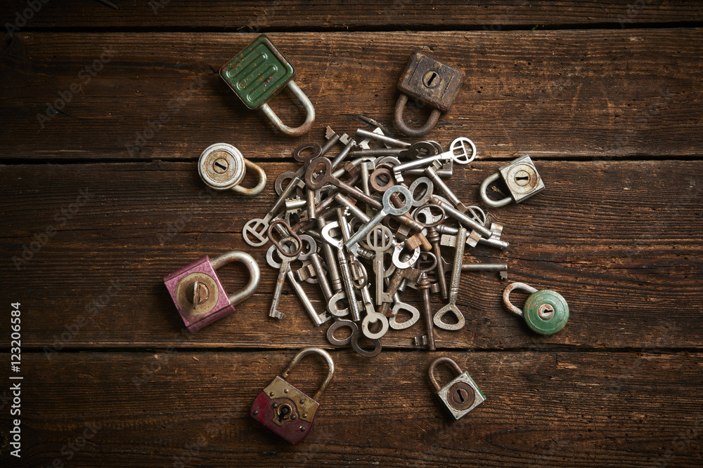 Group of old rusty padlocks with pile of keys on brown wooden table

