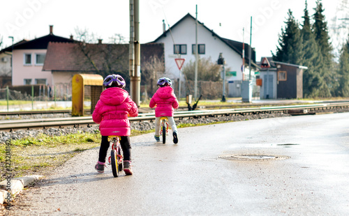 Twins children riding balance bikes on the road with helmet.