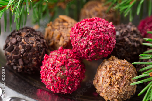 Assorted dark chocolate truffles with dried strawberry pieces and chopped hazelnuts on rustic wooden background