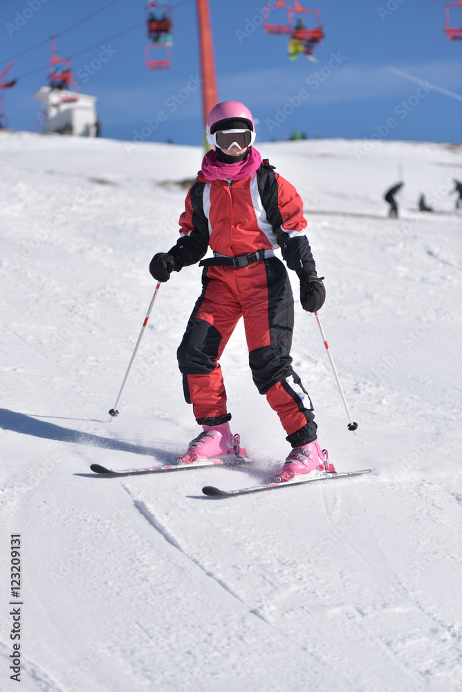 Young woman skiing downhill with blue sky and chairlift in the background