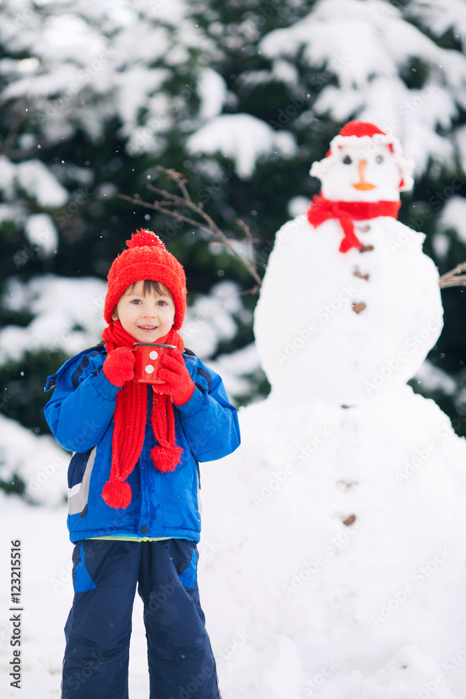 Happy beautiful child building snowman in garden Happy beautiful child building snowman in garden
