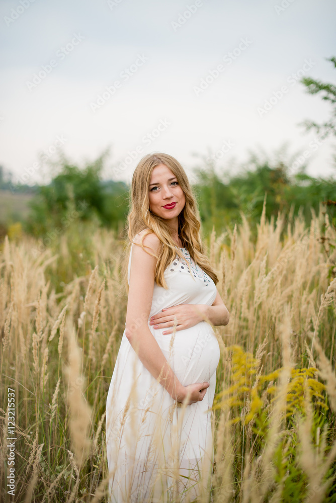 Happy and yonge pregnant woman in a white dress with long blond hair in tall grass Happy and yonge pregnant woman in a white dress with long blond hair in tall grass