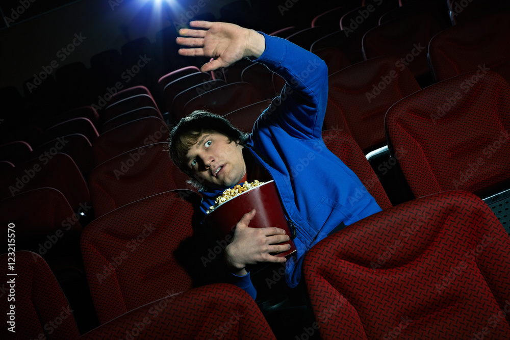 Naklejka premium Young man is terrified by the scene seen on the screen in cinema hall 