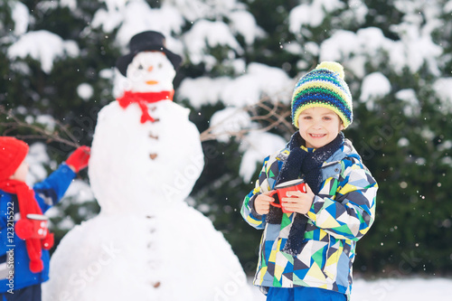 Happy beautiful children, brothers, building snowman in garden a