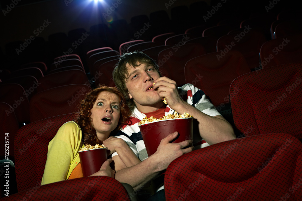 Naklejka premium Young girl embracing her boyfriend terrified by the movie