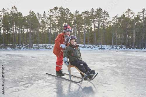 Boy pushing friend on kicksled across frozen lake, Gavle, Sweden photo