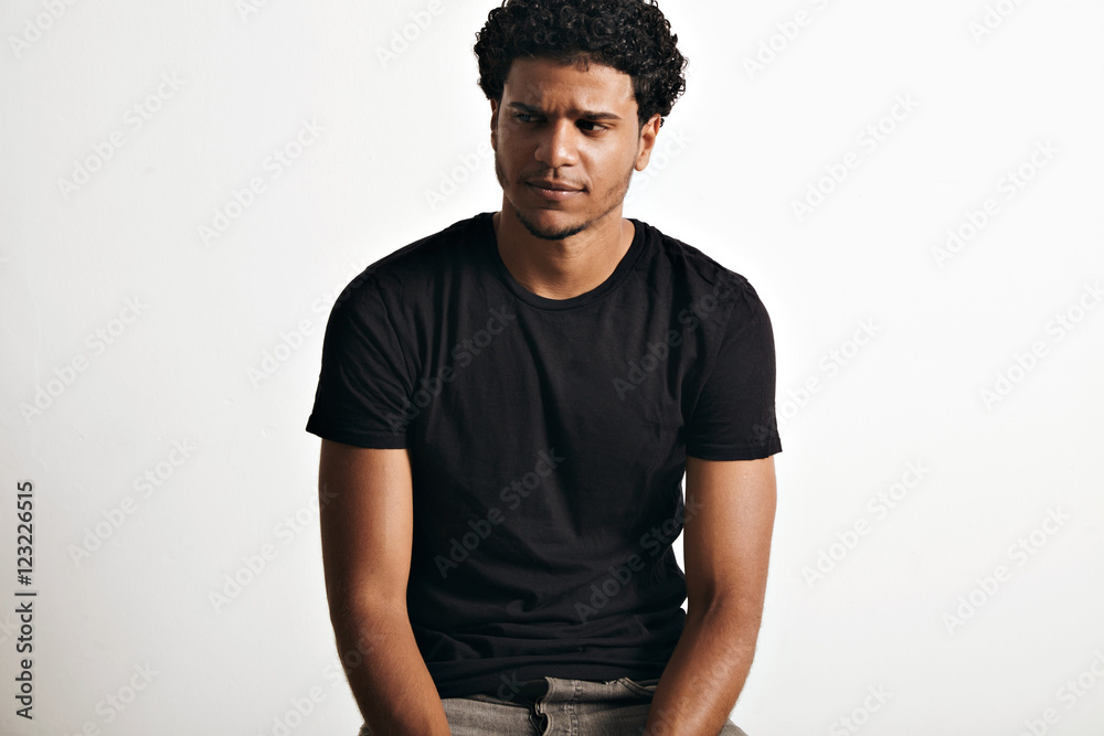 Ironic thoughtful handsome young man with an afro wearing a black sleeveless cotton t-shirt against white wall background Ironic thoughtful handsome young man with an afro wearing a black sleeveless cotton t-shirt against white wall background