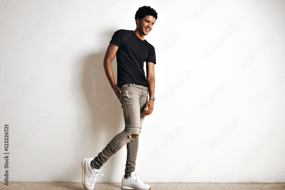 Full body shot of a cute tall young African American model with an afro in  a plain black cotton t-shirt, white sneakers and slim grey jeans isolated  on white Stock Photo