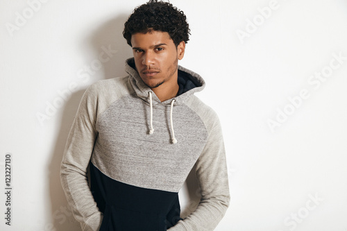 Young attractive latino guy wearing blank grey sweatshot with hood, looking suspiciously on camera, isolated on white photo