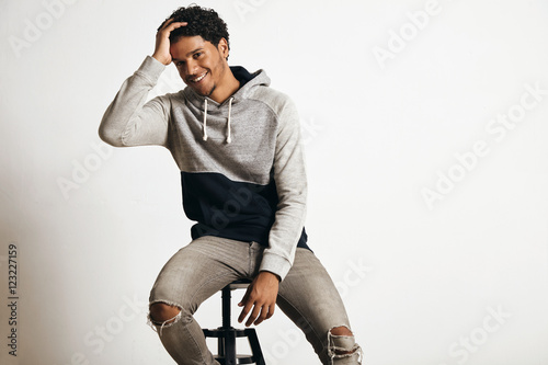 Happy smiling joyful attractive black guy sits on high bar chair in blank grey sweat hoodie and poses looking at camera