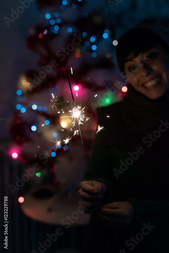 Young handsome caucasian short brown hair woman celebrating holding a sparkler, looking the flame, smiling - celebrating, new year eve, happiness