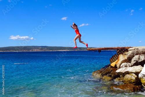 Teenage girl jumping into the sea on the sun