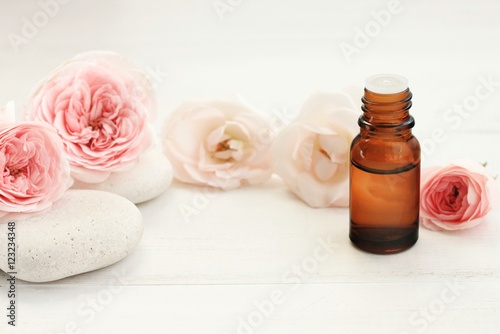 Rose essential oil, fresh pastel colored flowers, spa stones, fragrant cosmetic line. Empty space for product display.