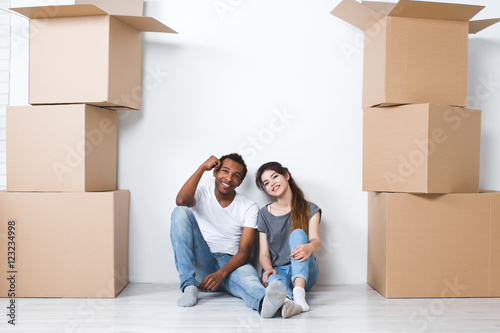 Portrait of happy young couple sitting on floor looking at camera and dreaming their new home and furnishing.