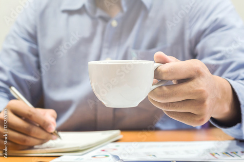 Businessman in a blue jacket with a cup of coffee in the cafe at the table, close-up