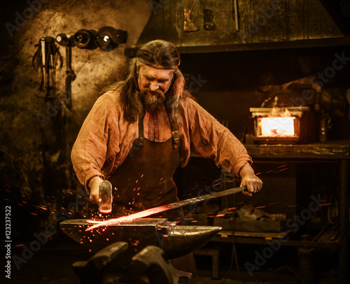 Senior blacksmith forging the molten metal on the anvil in smithy