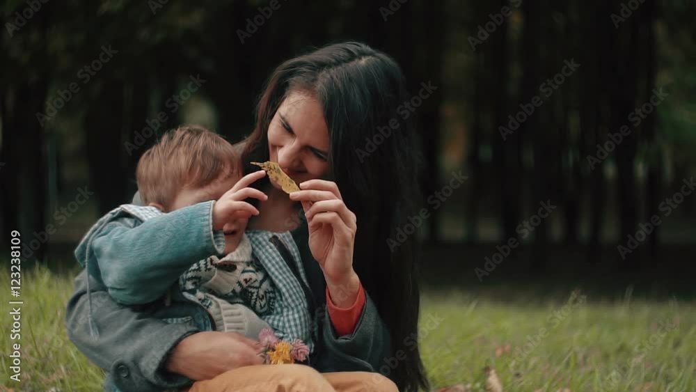 young beautiful mother playing with her cute little son, who is sitting on her lap in the autumn park young beautiful mother playing with her cute little son, who is sitting on her lap in the autumn park
