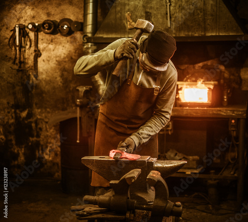 The blacksmith forging the molten metal on the anvil in smithy photo