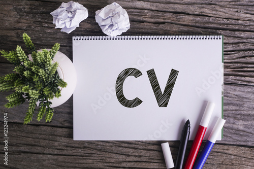 Notepad and green plant on wooden background with CV word.