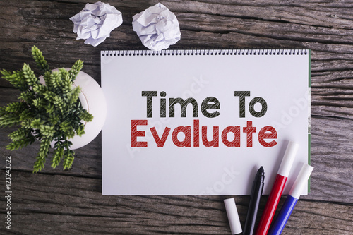 Notepad and green plant on wooden background with Time To Evaluate