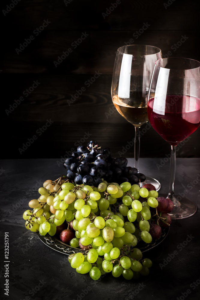 Wine in glasses and different types of grape on dark background.