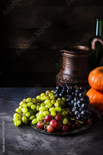 Wine in jug and different types of grape on dark background.