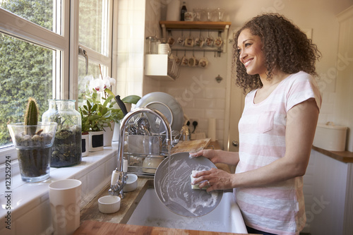 Woman Standing At Kitchen Sink Washing Up