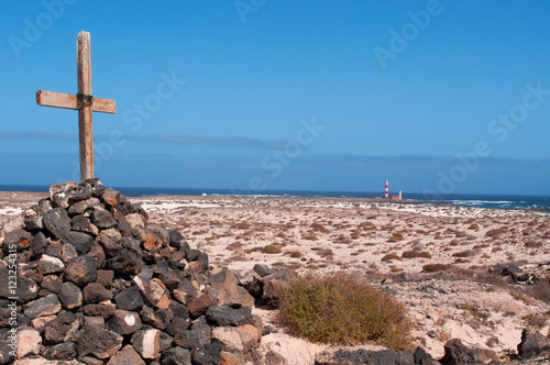 Fuerteventura, Isole Canarie: una croce di legno su una pila di sassi e il faro del Toston, vicino al villaggio di pescatori di El Cotillo, il 3 settembre 2016 © Naeblys