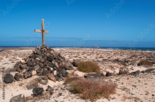 Fuerteventura, Isole Canarie: una croce di legno su una pila di sassi e il faro del Toston, vicino al villaggio di pescatori di El Cotillo, il 3 settembre 2016 photo