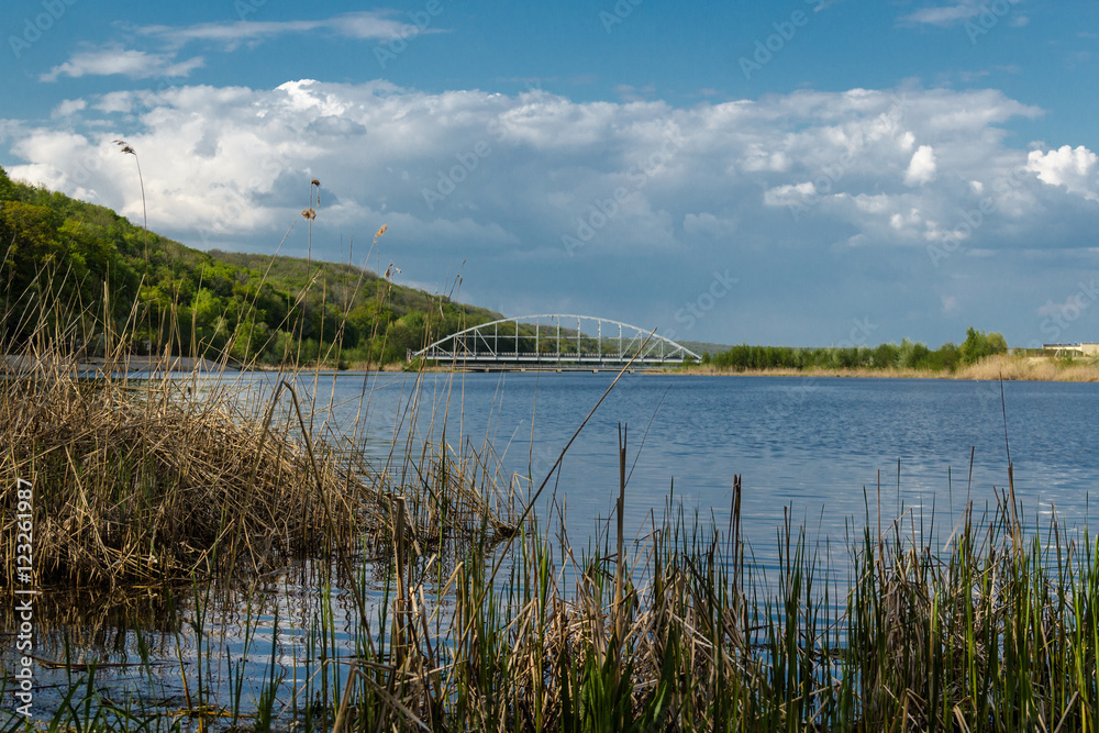 A beautiful Blue Lake with yellow grass in the foreground and a blue sky with clouds