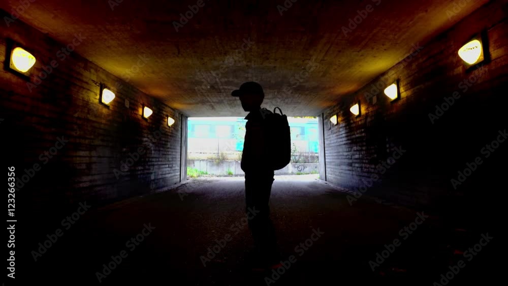 Silhouette of a boy walking in a dark tunnel with a train passing by the end of the tunnel. Silhouette of a boy walking in a dark tunnel with a train passing by the end of the tunnel.