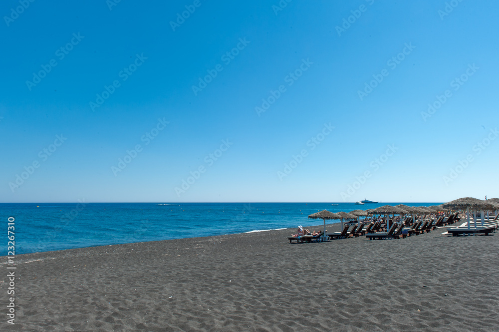 Fototapeta premium The people sunbathing on the black beach of Kamari in Santorini, Greece.