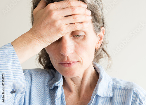 Close up of middle aged woman iwith hand on forehead covering one eye photo