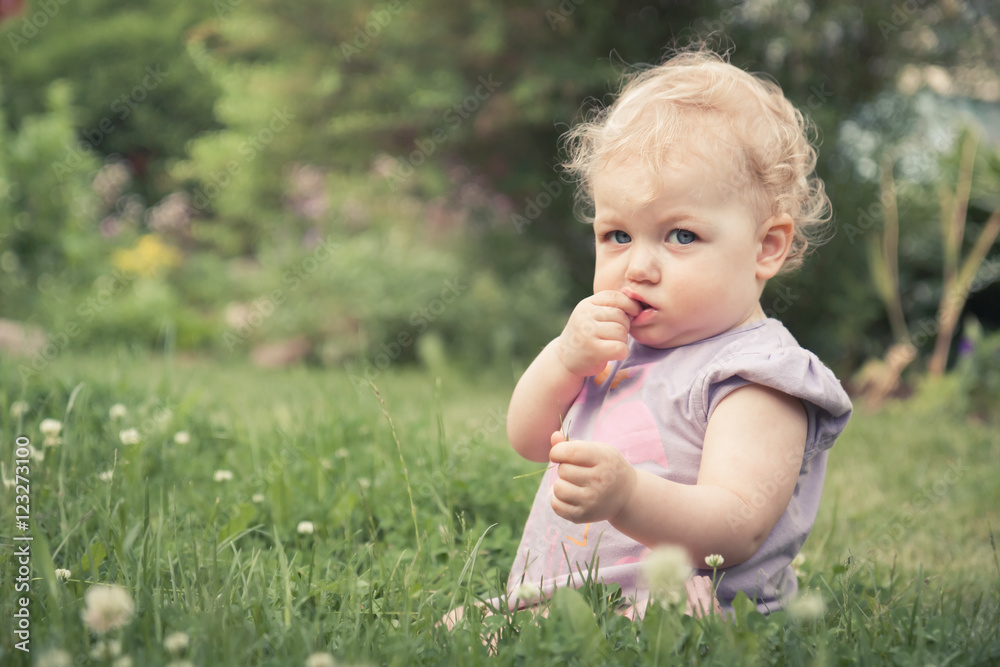 Cute baby girl sitting in grass among blossoming flowers in summer park with copy space Cute baby girl sitting in grass among blossoming flowers in summer park with copy space