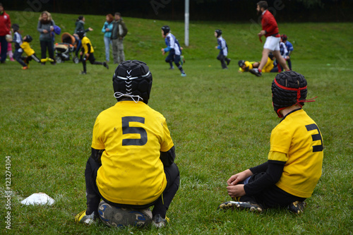 Two young rugby players in yellow shirts are watching match