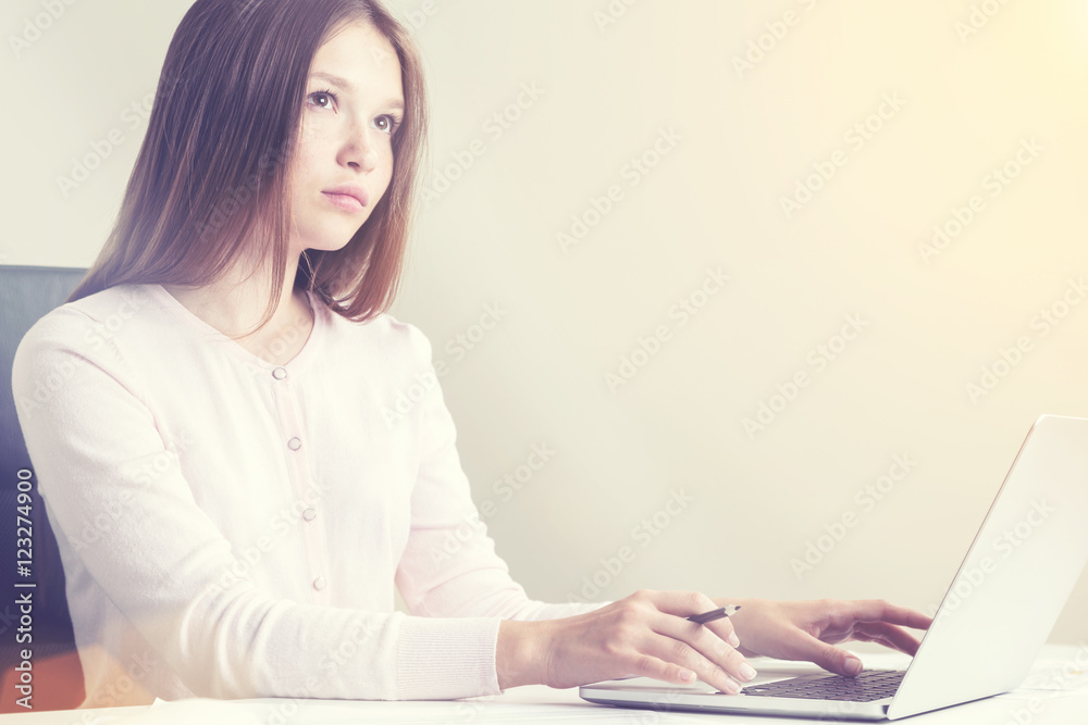 Thoughtful female using laptop in sunlit office Thoughtful female using laptop in sunlit office