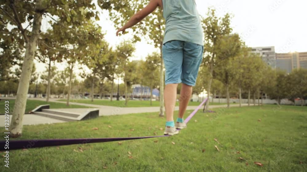 Guy walks on slackline at public park
