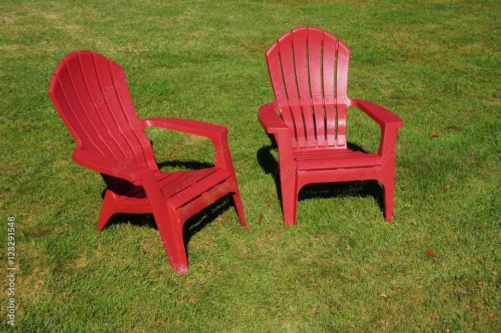 Two red Adirondack chairs in the grass